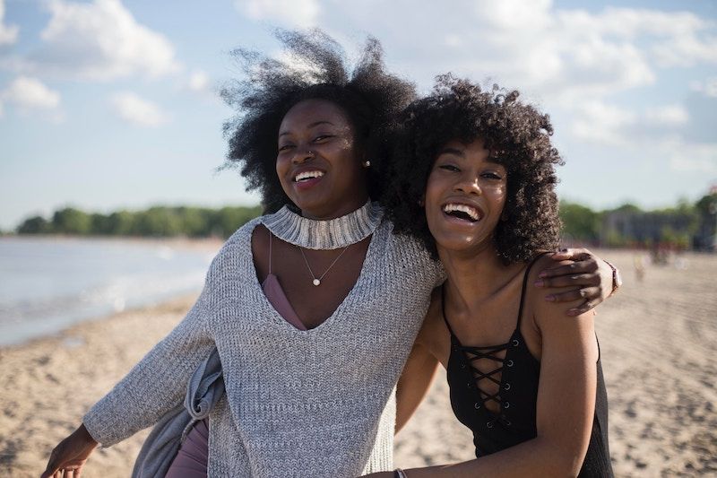 Two adult dark skinned woman embracing each other on the beach