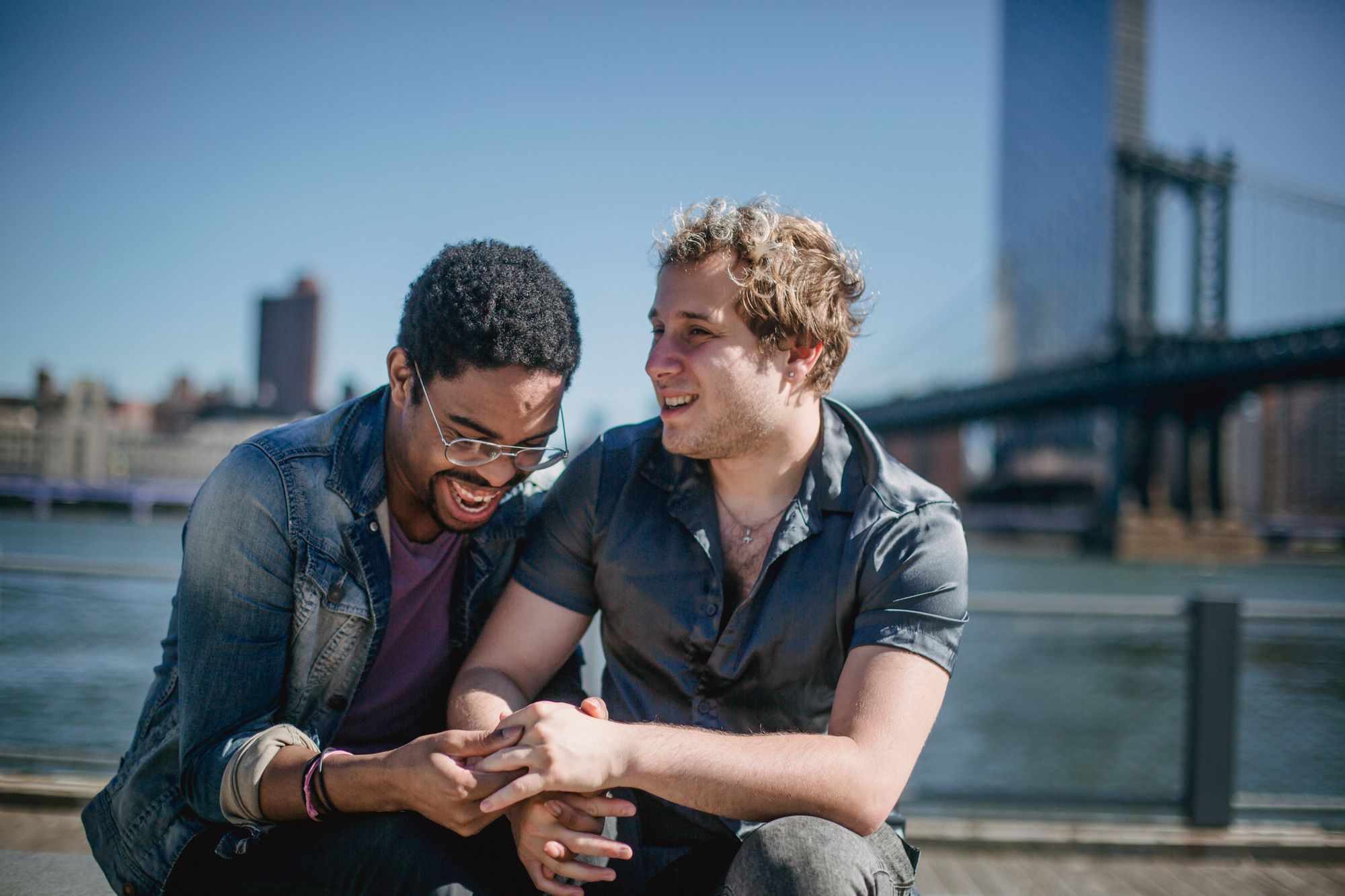 Gay couple sitting by river in front of bridge