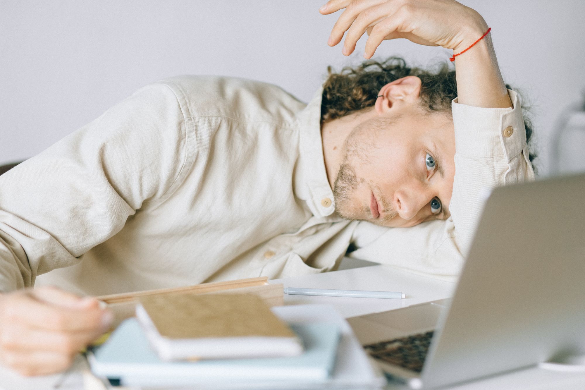 A adult sitting with their head down at a desk in front of a laptop