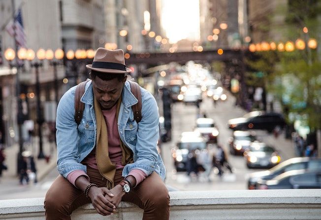 Dark skinned man sitting on a ledge with a cityscape behind him