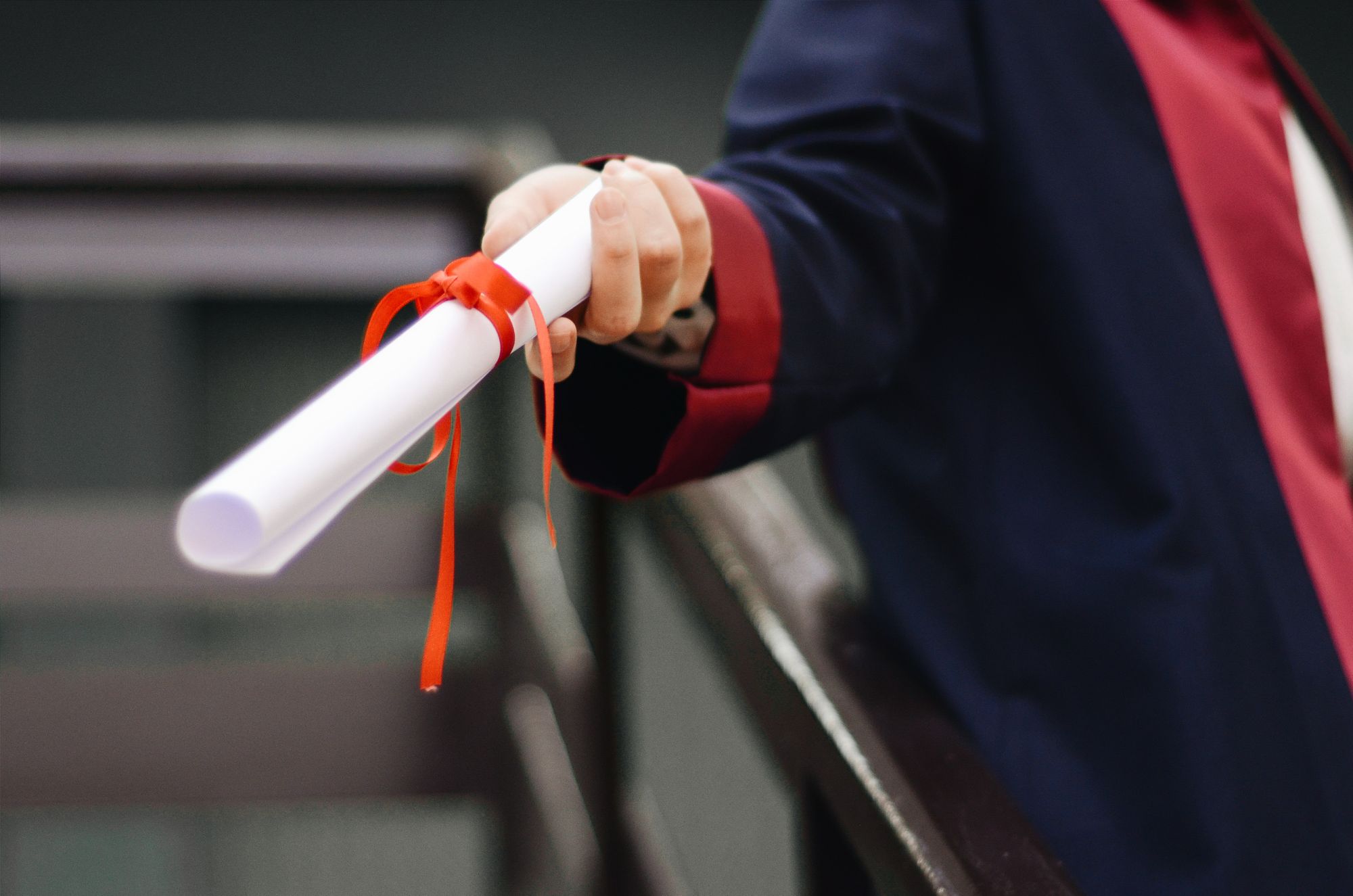Light skinned person handing out a diploma wrapped in orange ribbon.