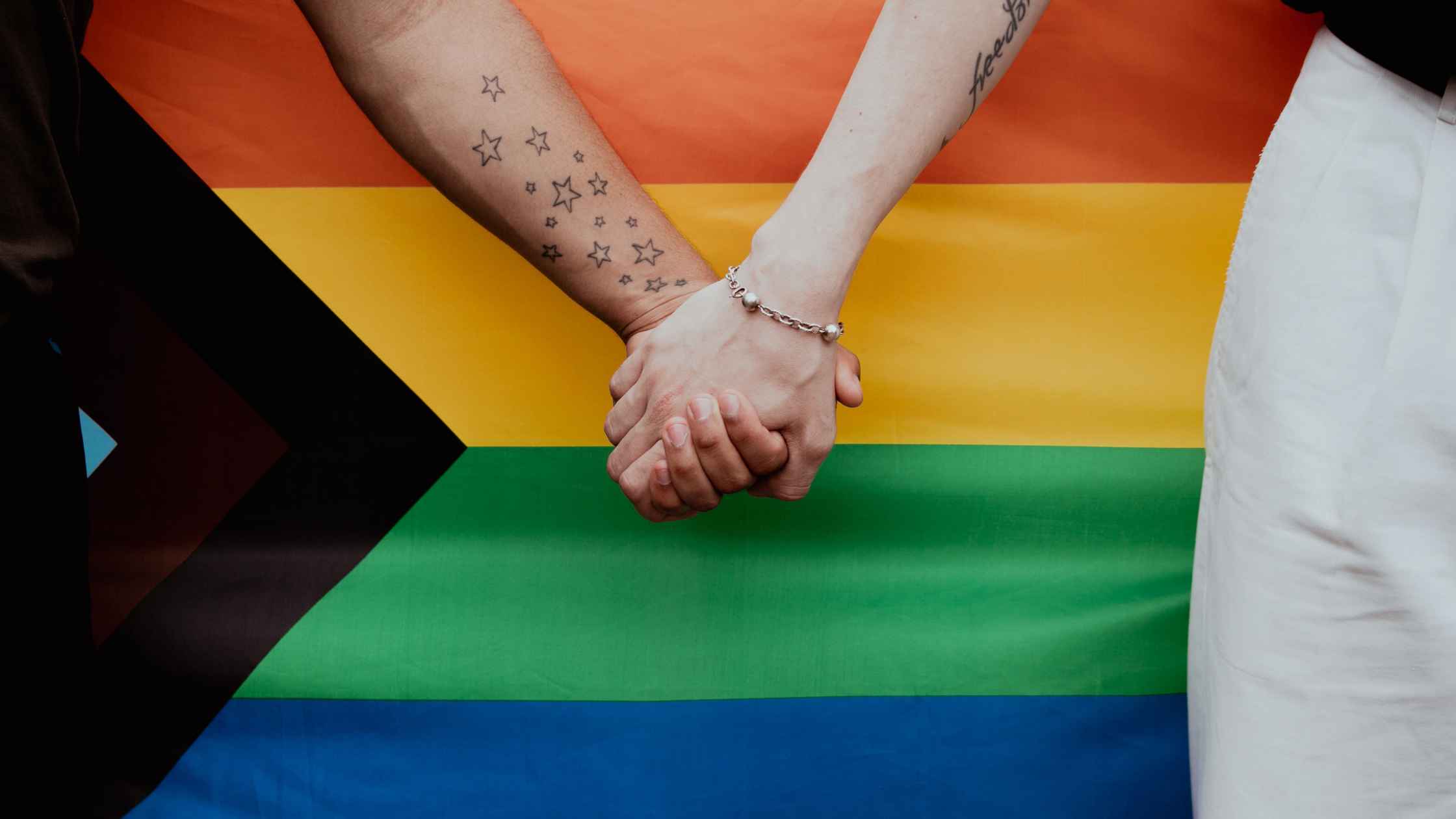 Couple holding hands in front of pride flag.