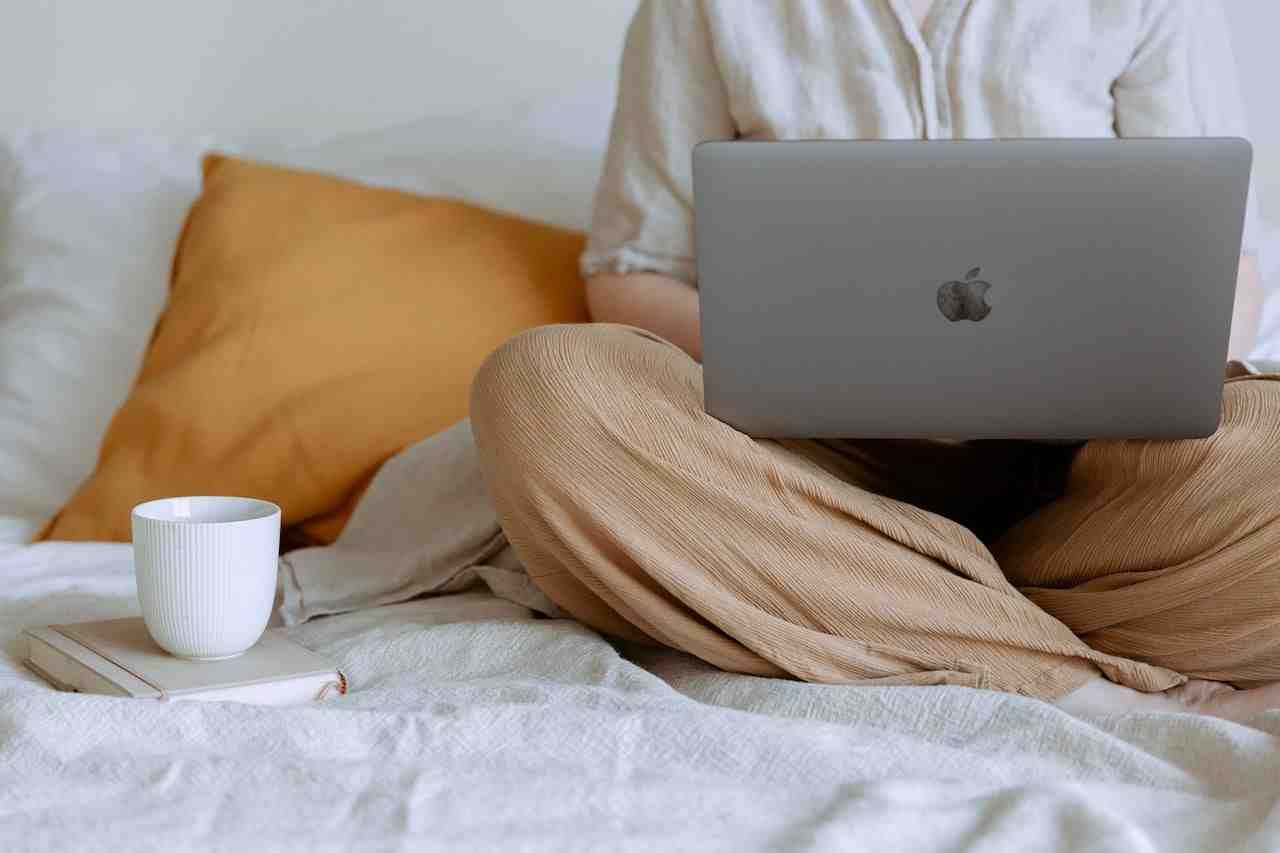 Women with orange pants sitting in bed with laptop open.