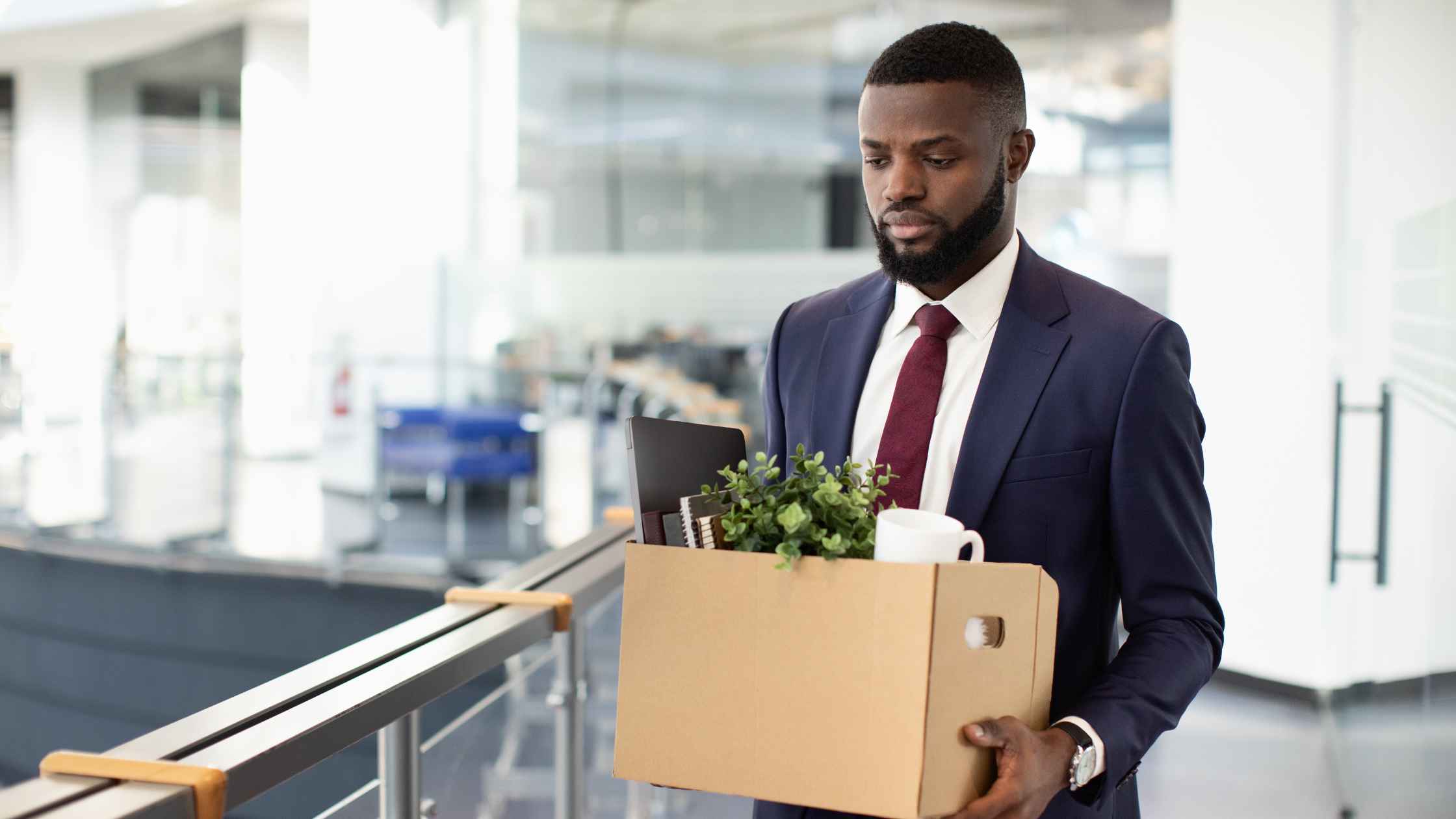 African American person in a suite leaving the office with a box of stuff as if laid off or fired
