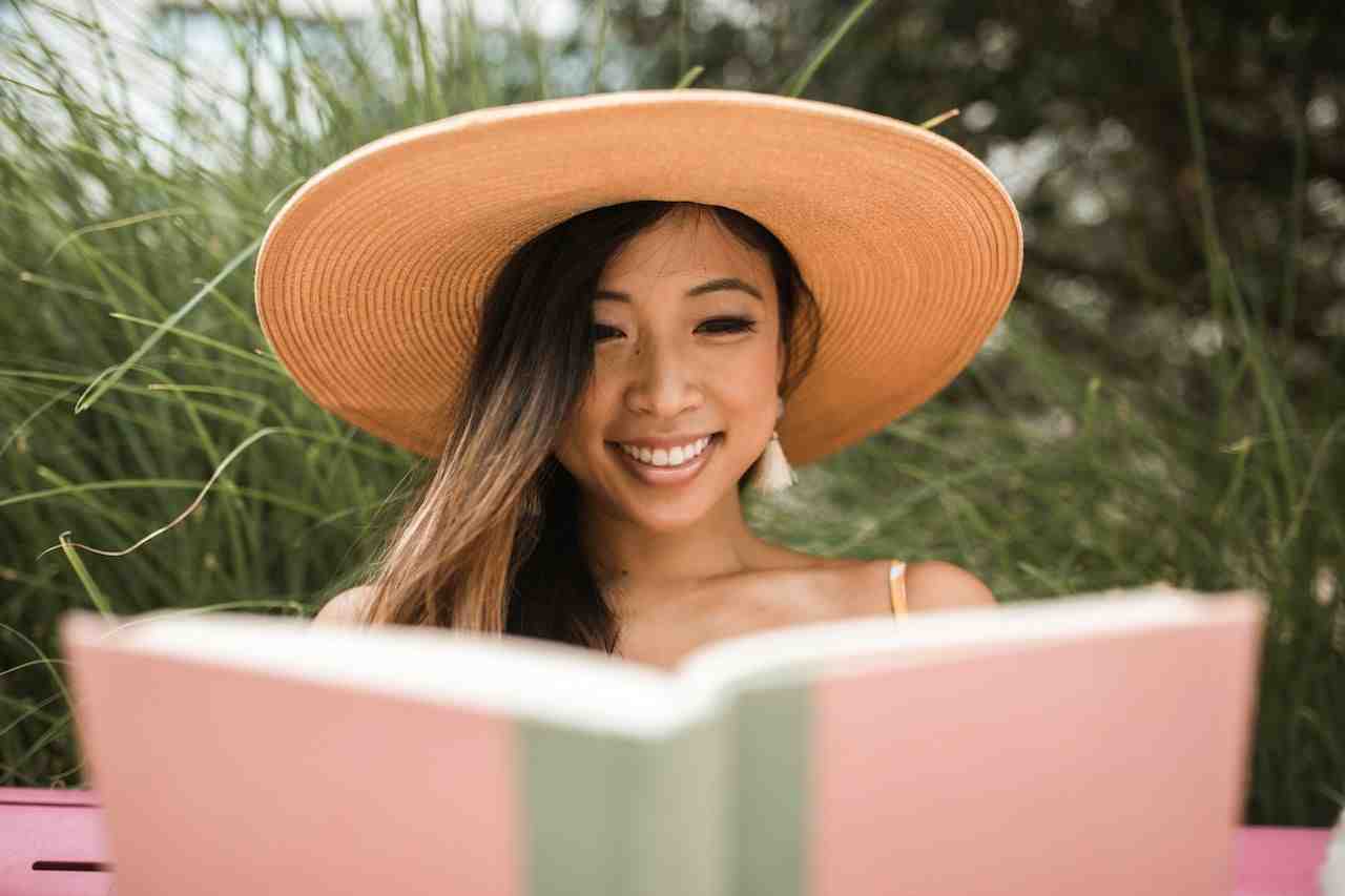 Women in large hat reading a book and smiling.