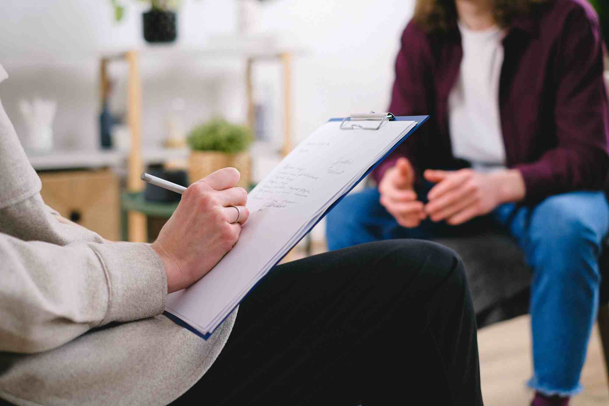 Close up of two Caucasian persons sitting across from one another while one talks and the other writes notes.