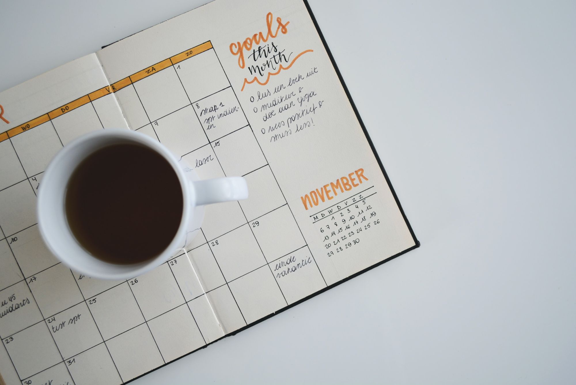 a cup of coffee sitting on top of a monthly planner that outlines goals