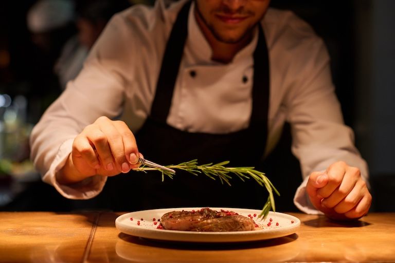 a chef plating a piece of meat with garnish