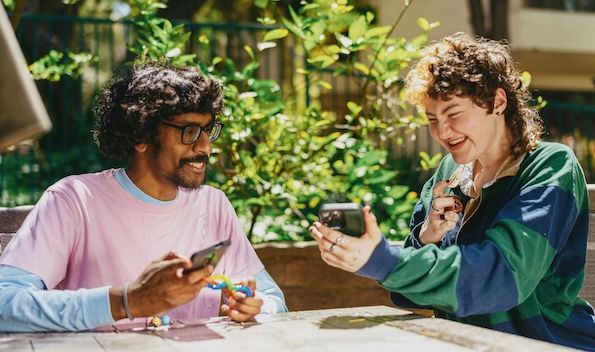 two friends sitting at a table laughing and sharing phones