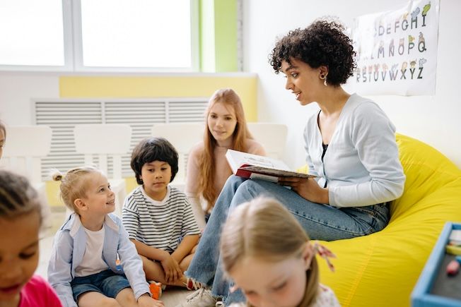 a teacher with short curly hair sitting and reading to children