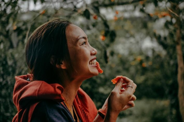 an adult eating an orange looking happy