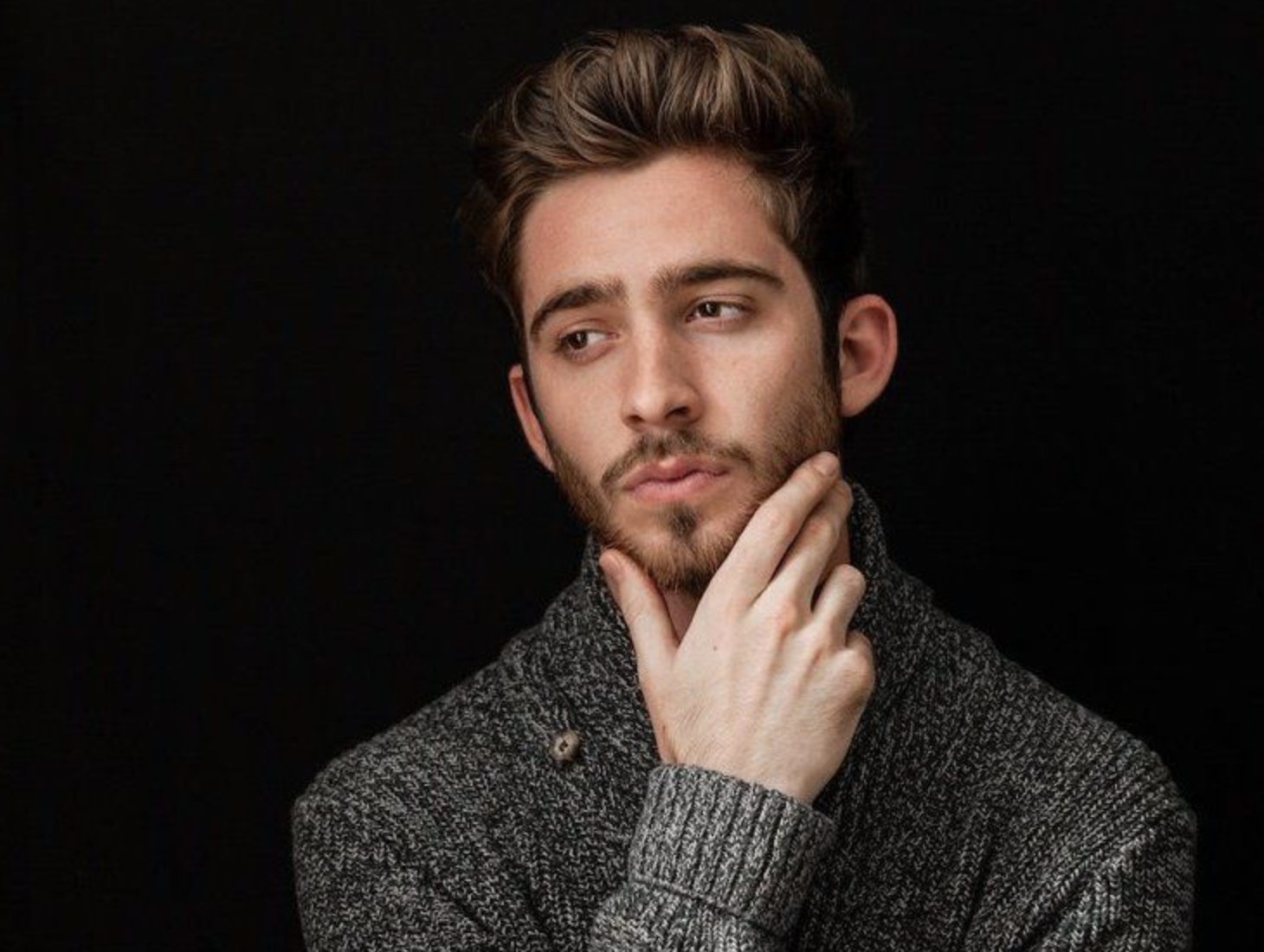 An adult with short brown hair and light skin, wearing a grey cardigan looking off to the side